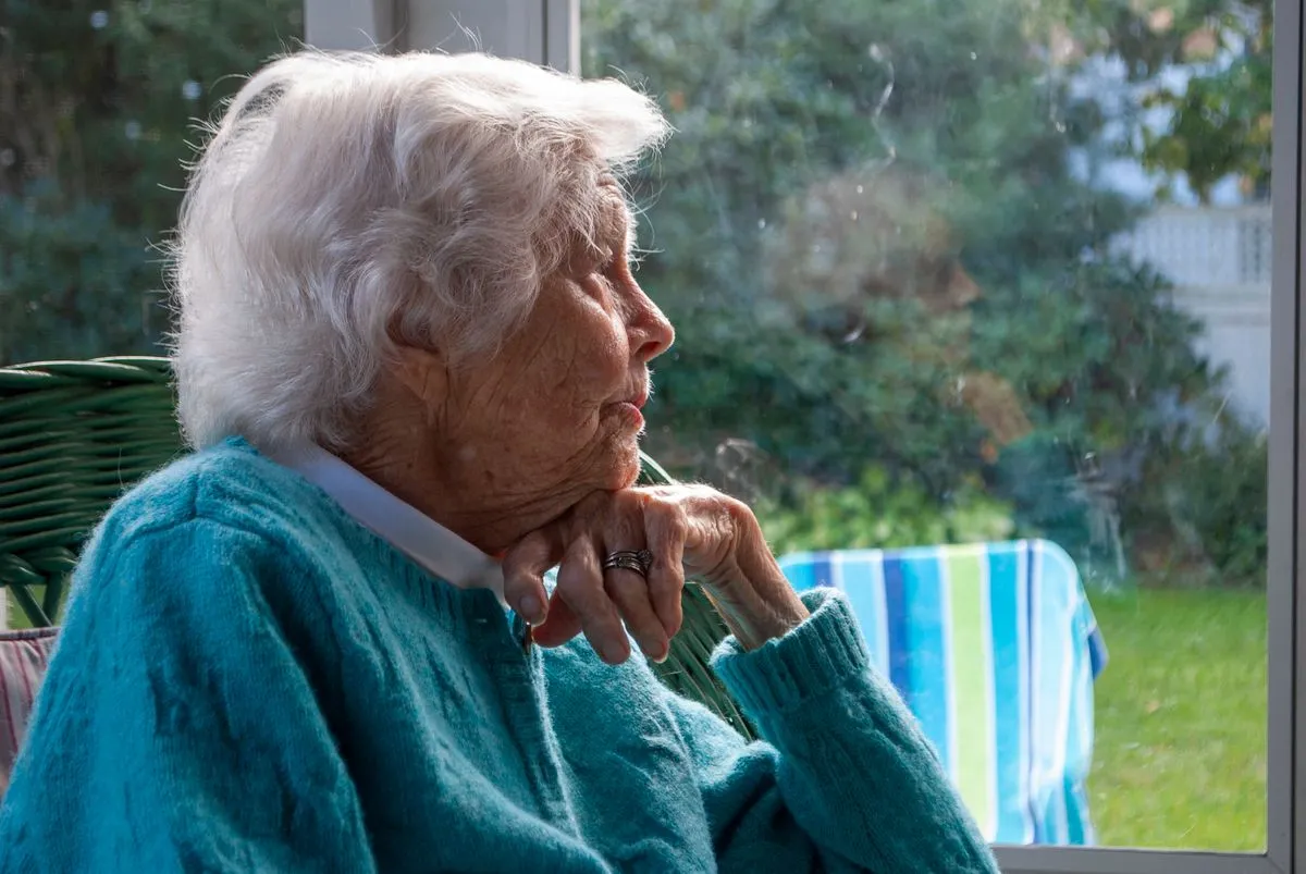 Elderly woman looking out of a window, reflecting quietly